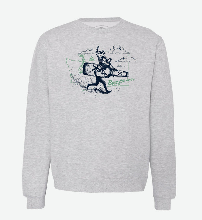 Heather grey crewneck sweatshirt by The Great PNW featuring a vintage graphic of a cowboy riding a giant running Rainier Beer bottle. The design includes a light green outline of Washington state in the background and the text "Beer for here." written in green cursive.