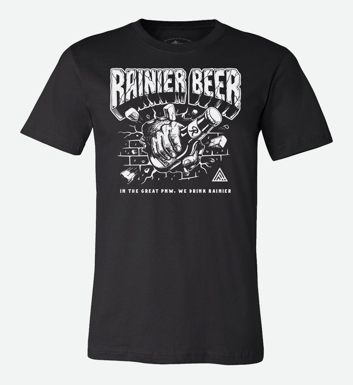 Black t-shirt by The Great PNW featuring a graphic illustration of a hairy Sasquatch hand holding a bottle of Rainier Beer and smashing through a brick wall. Bold text reads "RAINIER BEER" at the top and "IN THE GREAT PNW, WE DRINK RAINIER" at the bottom.